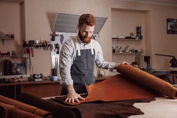 Fototapeta Shoemaker tailor hold different rolls natural brown leather, working with textile in workshop obraz