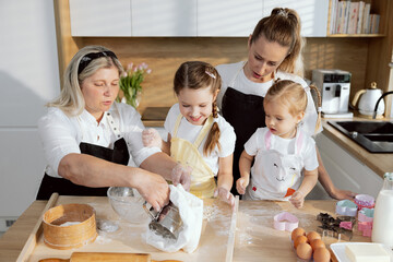 Granny showing how correctly collecting flour in sieve and sifting through sieve. Delihted grandchildren watching carefully wanting try to do. Baking cooking in the kitchen, women having fun together.