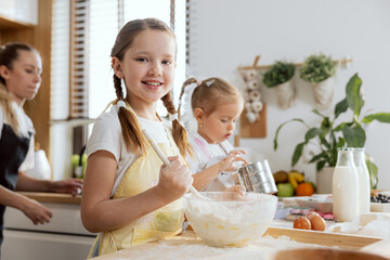 Close-up shot curious beautiful girl wearing apron kneading dough holding spoon in hand smiling at...
