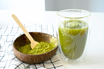 Matcha green tea in a double-bottomed glass with a coconut bowl filled with matcha powder on a white background.