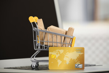 Online payment concept. Small shopping cart with bank card, boxes on laptop, closeup