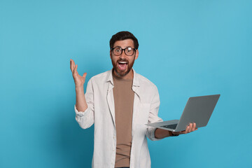 Emotional man with laptop on light blue background