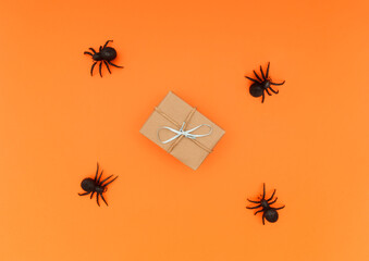 Some black toy spiders and a gift box with ribbon. Orange background