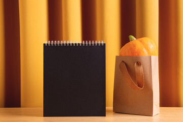 Autumn, fall season, Halloween mockup with traditional holiday orange natural pumpkin in eco friendly shopping bag and black paper card with blank space for your text. Front view, studio shot. 