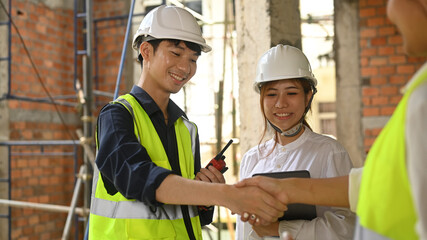 Smiling asian engineer and investor shaking hands for real estate project, agreement success in working site