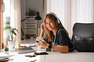 Beautiful asian woman listening to music with wireless headphones and using mobile phone her workplace