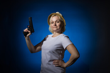 Adult woman in a hat with a gun on a dark background.