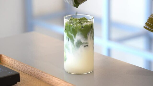 Preparation of summer refreshing beverage iced matcha latte, pouring matcha green tea mix into a glass of fresh full cream milk, cinematic close up shot.