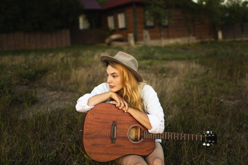A girl with a guitar in her hands sits on the grass and plays and sings. The girl plays the...