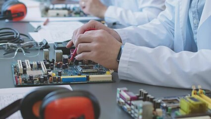 Unrecognizable electronics engineer soldering motherboard parts at desk in laboratory - Powered by Adobe