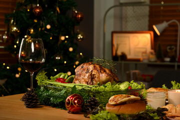 Thanksgiving table with roasted turkey, red wine and sides dishes in decorated room with a Christmas tree