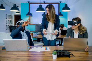 Multiracial coworkers using tablet laptops and VR goggles in office