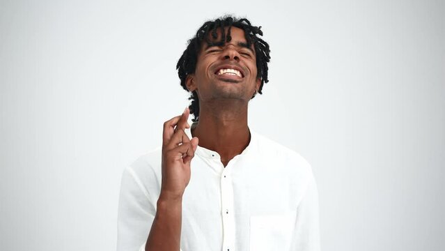 Smiling African man with dreadlocks hoping for something with crossed fingers in the white studio