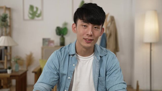 webcam view of an Asian male manager nodding head while listening attentively to coworker&rsquo;s ideas in a video conference while working from home in living room