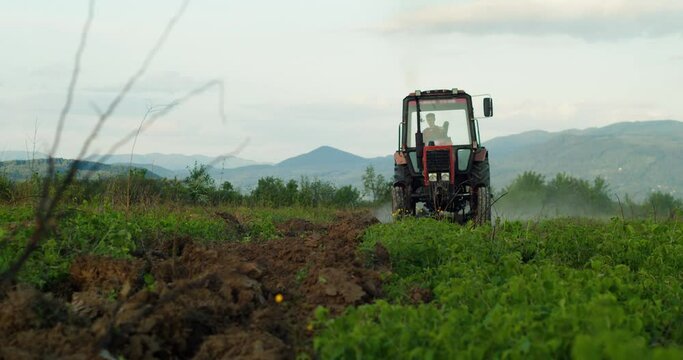 Tractor driver finished work after a hard day's work. Tractor harvests against the backdrop of high mountains at sunset