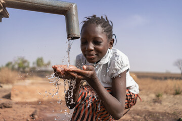 Close-up of an African girl collecting water from a village tap in an arid equatorial area; climate...
