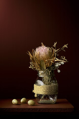 Dried protea flower arrangement in glass pot with quail eggs on the side