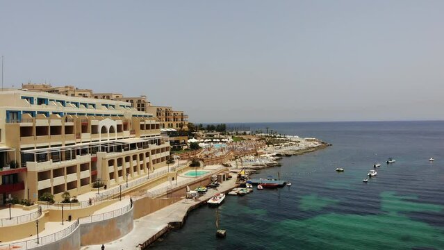 Aerial view of calm waves and emerald blue mediterranean sea next to Marina Hotel Corinthia Beach Resort coastline in Saint George's Bay, St Julian's, Malta.