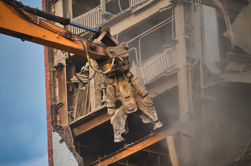 Hydraulic cutter of crane demolishes old industrial building