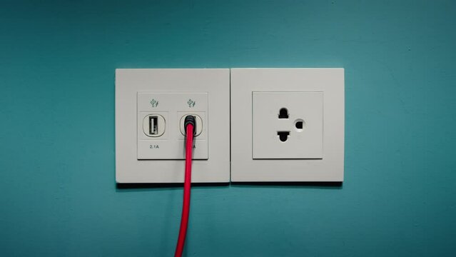 A man's hand was connecting an electrical appliance in his house. A man inserts a usb cable into a socket to charge his phone