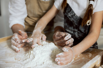 Close-up shot kid's hands and man's playing with flour on wooden surface. Sieving kneading process.