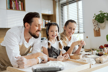 Happy young family in modern kitchen spending time together looking t camera smiling wearing...
