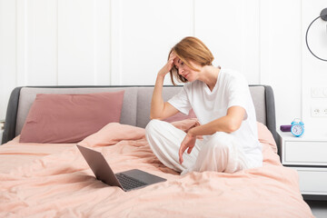 Attractive woman sitting on bed and working on  laptop in the bedroom at the morning time