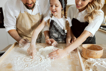 Close-up shot of drawing heart with flour. Happy mother and father teaching young adorable daughter...