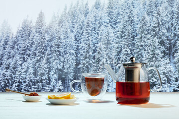 Kettle and two cups of delicious black tea with honey and lemons on winter forest background