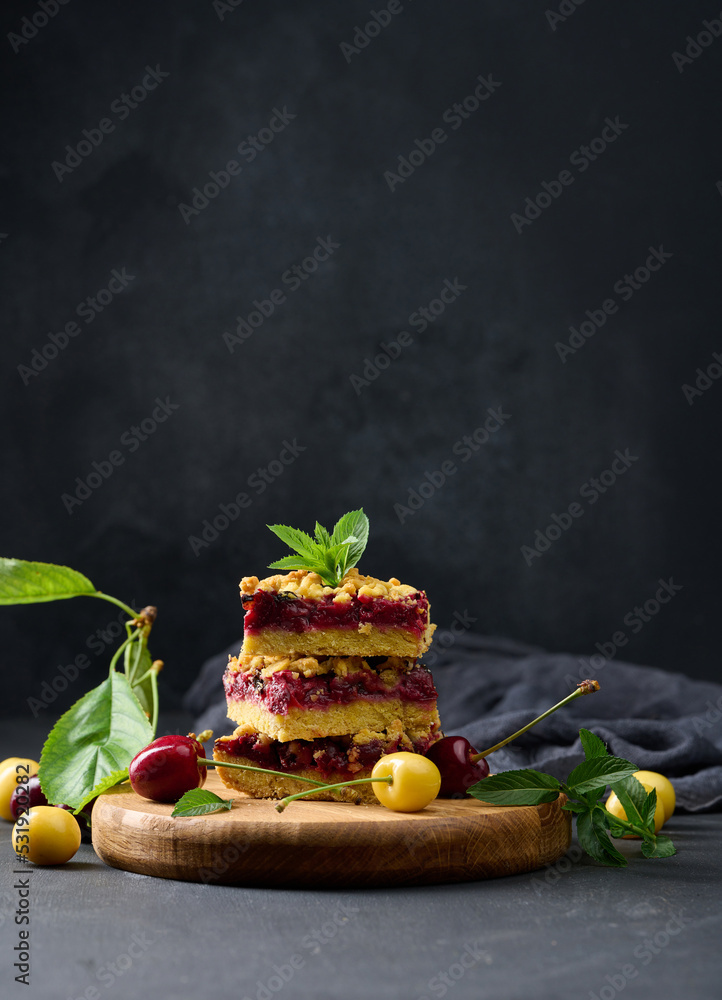Poster square slices of cherry crumble lie in a stack on a black background.