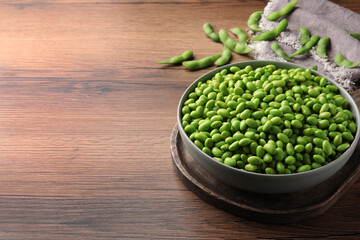 Bowl of delicious edamame beans on wooden table, space for text