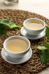 Green tea in white cups with leaves and wicker mat on table