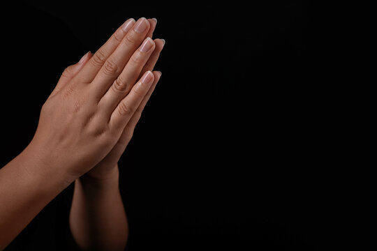 Woman holding hands clasped while praying against black background, closeup. Space for text