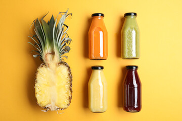 Bottles with delicious colorful juices and cut pineapple on yellow background, flat lay