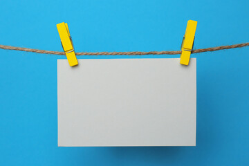 Wooden clothespins with blank notepaper on twine against light blue background. Space for text