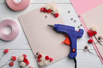 Flat lay composition with hot glue gun on white wooden table. Space for text