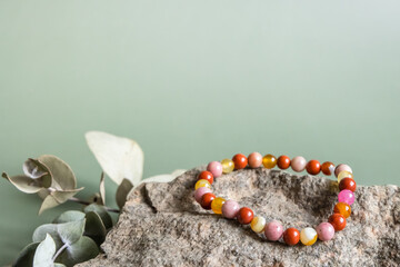 Bracelet made of natural pink agate stones beads on green background. Handmade jewelry. Woman...