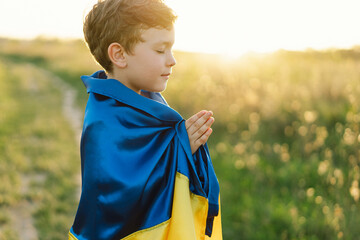 Ukrainian boy closed her eyes and praying to stop the war in Ukraine in a field at sunset. Hands folded in prayer concept for faith, spirituality and religion. War of Russia against Ukraine. Stop War