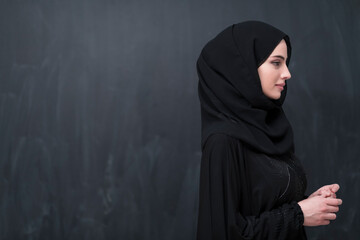 Portrait of beautiful muslim woman in fashionable dress with hijab in front of black chalkboard representing modern islam fashion and ramadan kareem concept