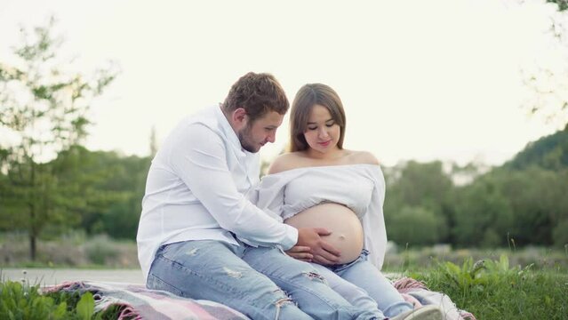 Pregnant girl and her boyfriend are hugging her tummy. Pregnancy and happiness young family. Future mother and father are waiting birth baby, their firstborn. Wife and husband are resting in the park.