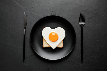 Tasty fried egg in shape of heart with toast served on black table, flat lay