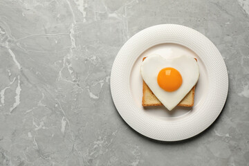 Plate with tasty fried egg in shape of heart and toast on marble table, top view. Space for text
