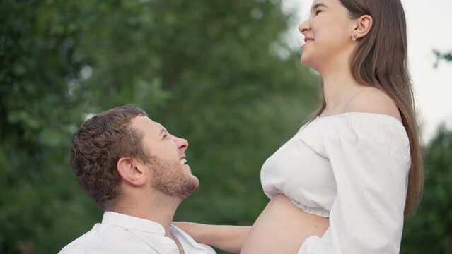 Pregnant girl and her boyfriend are hugging her tummy. Pregnancy and happiness young family. Future mother and father are waiting birth baby, their firstborn. Wife and husband are resting in the park.