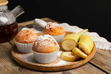 Obraz na płótnie Canvas Tasty muffins served with banana slices on wooden table against dark background