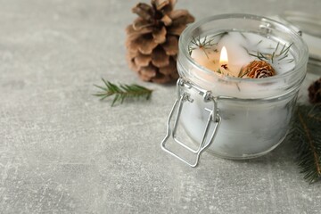 Fototapeta na wymiar Burning scented conifer candle and Christmas decor on grey table. Space for text