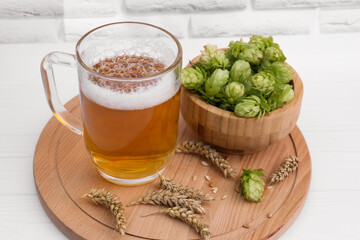 Mug with beer, fresh hops and ears of wheat on white wooden table