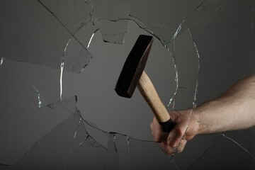 Man breaking window with hammer on grey background, closeup