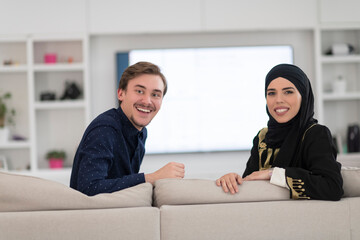 Young muslim couple woman wearing islamic hijab clothes sitting on sofa watching TV together during the month of Ramadan at modern home
