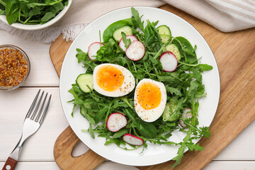 Delicious salad with boiled egg, vegetables and arugula served on white wooden table, flat lay