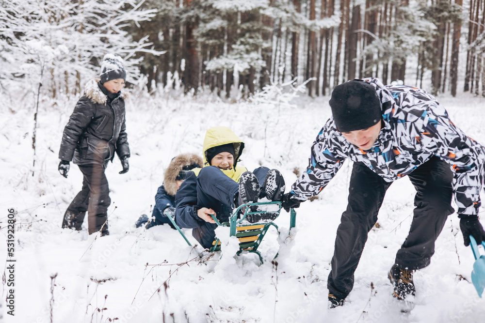 Wall mural Father and sons sledding and having fun together winter forest. Happy children and young man playing in snow. Teenager boys, cute toddler walking on frosty day. Wintertime activity outdoors